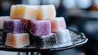 Colorful sugar-coated Turkish delight cubes arranged on dark ceramic plate, soft focus macro shot with selective depth of field and bokeh background.