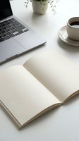 Clean minimalist workspace with open blank notebook, laptop, coffee cup and plant on white desk for productivity and planning.