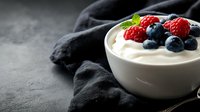 Fresh berries on top of creamy yogurt or dessert in white ceramic bowl against dark background with black textile, healthy breakfast concept.