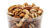 Mixed nuts assortment in glass bowl with walnuts, almonds, cashews, pistachios and pecans isolated on white background for healthy snacking and cooking.