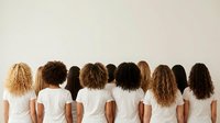 Diverse group of women with different natural hair textures and ethnicities wearing white t-shirts, standing with backs turned showing variety of curly, wavy and straight hairstyles.