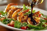 Grilled shrimp salad with fresh greens, tomatoes and balsamic vinaigrette dressing being poured over seafood dish.