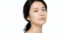 Young Asian woman with natural makeup and healthy glowing skin looking up thoughtfully against white background for beauty and skincare concepts.