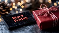 Red wrapped gift box with twine bow next to Black Friday sale tag against blurred bokeh lights background, creating festive holiday shopping atmosphere.