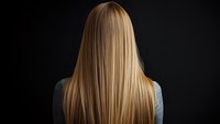Back view of straight blonde hair on dark background, showing healthy, smooth texture and natural highlights. Professional salon and beauty concept.