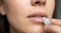 Woman applying clear lip balm to soft pink lips for moisturizing skincare routine and lip care maintenance.