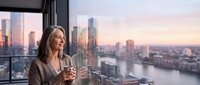 Professional businesswoman enjoying coffee while admiring city skyline from modern office window during golden hour sunset creating peaceful moment.