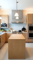 Modern kitchen interior with light wood cabinets, stainless steel appliances and pendant lighting for contemporary home design and renovation projects.