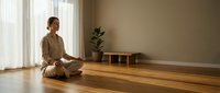 Young woman practicing mindfulness meditation in serene modern living room with natural light and wooden floors for wellness and mental health.