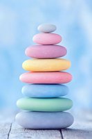 Balanced stack of smooth pastel-colored stones on wooden surface against soft blue background, creating zen-like harmony and peaceful composition.
