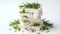 Fresh goat cheese rounds stacked with aromatic herbs rosemary thyme oregano and black pepper on white background for culinary cooking recipes.