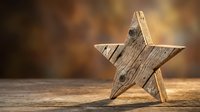 Rustic wooden star decoration on weathered wood surface with warm bokeh background for holiday crafts and seasonal home decor projects.