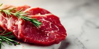 Fresh raw beef steak with rosemary herbs on marble surface ready for cooking. Premium red meat cut garnished with aromatic spices for culinary preparation.