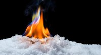 Fire flame burning through white snow on black background creating dramatic contrast between hot and cold elements for creative projects.