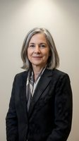 Professional mature businesswoman with gray hair in dark suit smiling confidently against neutral background for corporate headshot and business portraits.