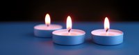 Three white tea light candles burning with bright flames on blue surface creating warm ambient lighting for relaxation and meditation atmosphere.
