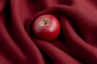 Fresh red apple on soft burgundy fabric with elegant folds creating a luxurious food styling composition for culinary or lifestyle content.