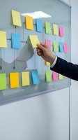 Business professional arranging colorful sticky notes on glass board for project planning, brainstorming, and workflow organization in modern office environment.