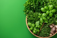 Fresh aromatic herbs and garlic in wooden bowl on green background, overhead view of basil, dill, parsley and spices for cooking Mediterranean cuisine.