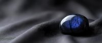 Polished labradorite gemstone with brilliant blue flash resting on smooth dark fabric surface creating elegant luxury jewelry display for premium accessories.