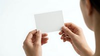 Person with medium skin tone holding blank white card or paper in both hands against white background, suitable for business card mockups, promotional materials, and corporate design templates.