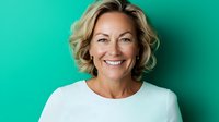 Confident mature blonde woman with bright genuine smile wearing white top against turquoise background, radiating positive professional energy and warmth.