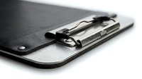 Black leather clipboard with metal clip mechanism for office documents and professional paperwork organization on white background.