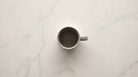 Empty white coffee cup on elegant marble surface viewed from above for minimalist kitchen and cafe design concepts.