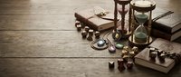 Vintage hourglass with antique brass compass, old books and wooden chess pieces on rustic table creating timeless atmosphere for educational content.