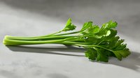 Fresh green celery stalks with leafy tops on neutral background for culinary and healthy eating concepts.