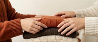 Supportive hands reaching together over folded warm sweaters, symbolizing care, comfort and human connection in cozy autumn winter clothing.