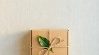 Kraft paper gift box wrapped with twine and fresh green leaf decoration on neutral background for eco-friendly packaging design.