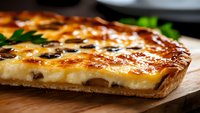 Homemade quiche with golden brown melted cheese crust and black olives on wooden cutting board, close up view showing flaky pastry texture and creamy filling.