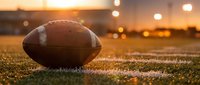 American football on grass field during golden hour sunset with stadium lights creating warm atmospheric sports scene for athletic competitions.