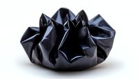 Crumpled black paper forms abstract sculptural shape against white background, creating dramatic shadows and highlights in minimalist artistic composition.