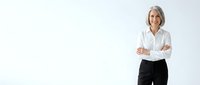 Confident mature businesswoman with crossed arms smiling in white shirt and black pants against clean background for corporate presentations.