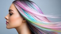 Young woman with vibrant rainbow colored hair in motion showing pink blue green yellow purple streaks against gray background for beauty salon advertising.