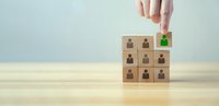 Hand selecting wooden cube with green checkmark from grid of business person icons representing recruitment and talent acquisition process.