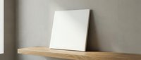 Blank white canvas leaning against beige wall on wooden shelf in minimalist interior space ready for artwork display and creative projects.