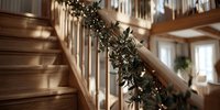 Wooden staircase with evergreen garland and string lights decorating handrail in cozy home interior during holiday season.