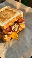 Grilled sandwich with melted cheese, crispy bacon and turkey on toasted bread served on parchment paper for breakfast or lunch menu.