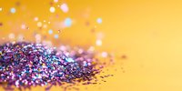 Sparkling purple and blue glitter scattered on yellow background with soft bokeh light effects, creating magical festive atmosphere for celebration designs.