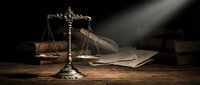 Vintage brass scales of justice with legal documents on wooden desk in dramatic lighting for law firm branding and legal services marketing materials.
