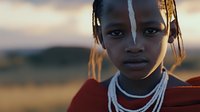 Young African woman with traditional beaded necklaces and braided hairstyle against sunset background, wearing red clothing. Soft golden light creates dramatic portrait.