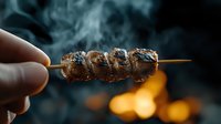Grilled meat skewer with charred seasoning held over open flame with rising smoke for barbecue cooking and outdoor dining concepts.