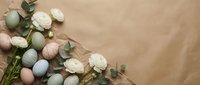 Easter eggs in pastel colors with white roses and eucalyptus branches arranged on beige background for spring holiday celebration and greeting cards.