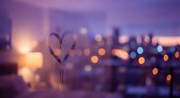 Heart shape drawn on foggy window glass with blurred city lights and purple sunset creating romantic urban evening atmosphere for love concepts.