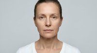 Middle-aged Caucasian woman with natural makeup-free skin showing aging signs, wearing white top against neutral background for skincare campaigns.