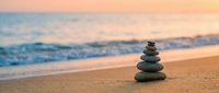 Zen stone stack on sandy beach at sunset with ocean waves and colorful sky creating peaceful meditation atmosphere for wellness and mindfulness practices.