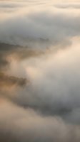 Misty mountain landscape with rolling hills shrouded in soft morning fog and warm golden light creating dreamy atmospheric layers for nature backgrounds.